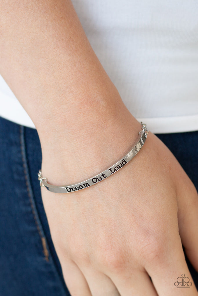A glistening silver chain attaches to a dainty silver bar stamped in the inspirational phrase, "Dream Out Loud", for a dreamy finish. Features an adjustable clasp closure.  Sold as one individual bracelet.