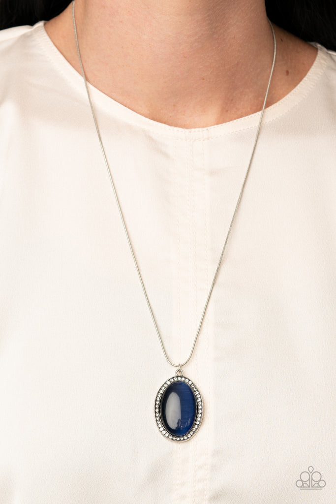 Encrusted with a ring of glittery white rhinestones, a wavy silver frame nestles around a glassy Blue Depths cat's eye stone. The dewy frame slides along a rounded silver snake chain, creating a glistening pendant below the collar. Features an adjustable clasp closure.  Sold as one individual necklace. Includes one pair of matching earrings.