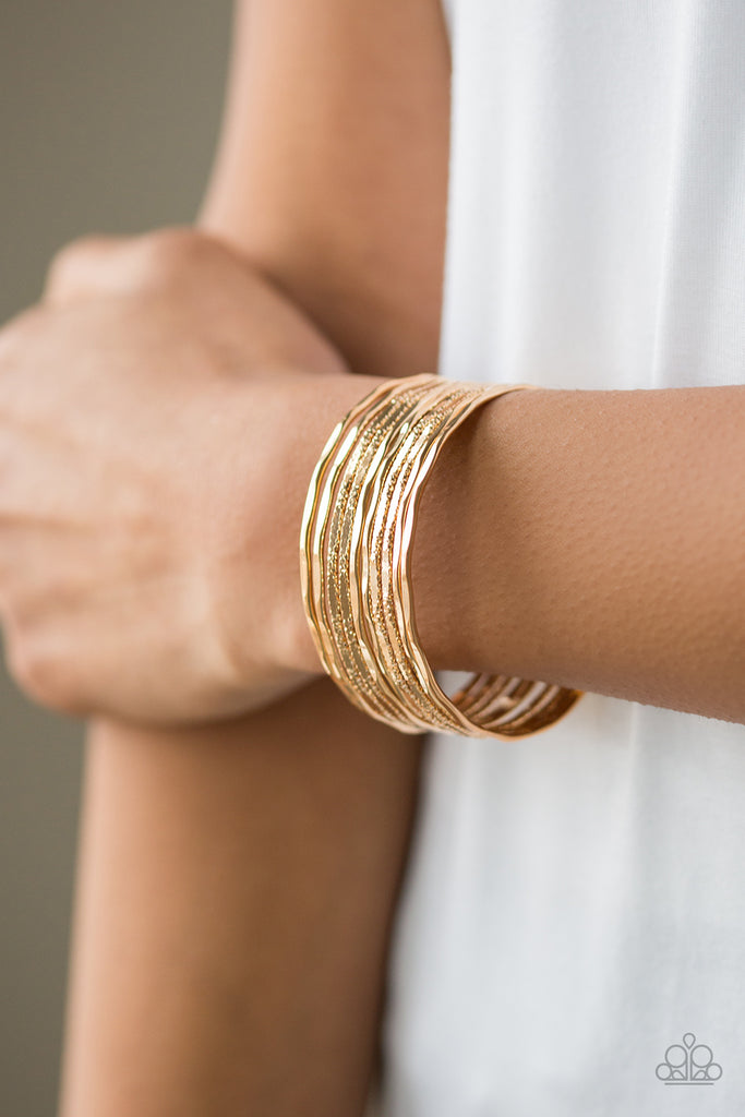 Sleek Shimmer Gold. Attached to two gold rods, a collection of faceted and hammered gold bars curl around the wrist, creating the illusion of stacked bangles.  Sold as one individual bracelet.