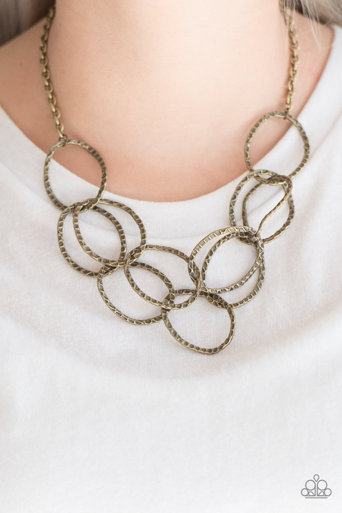 Asymmetrical brass rings have been delicately hammered with light catching shimmer. The glistening rings link below the collar, interlocking into two layered rows for an edgy finish. Features an adjustable clasp closure. Sold as one individual necklace.  Includes matching set of earrings as shown.  
