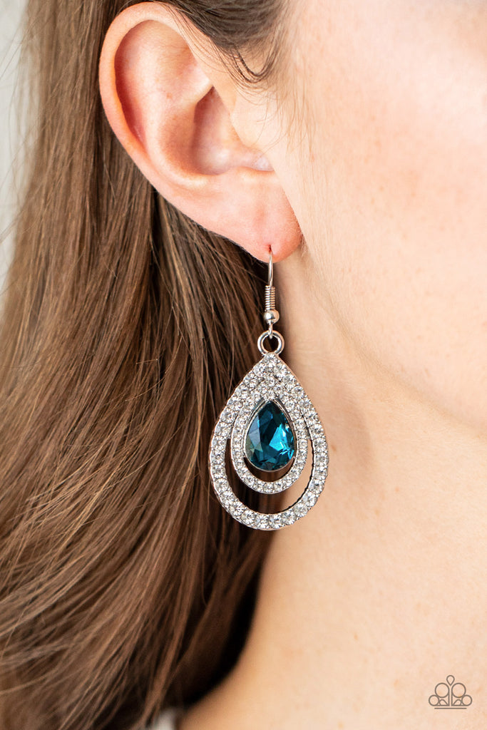 An oversized blue teardrop gem is nestled inside two expansive teardrop frames encrusted in dainty white rhinestones, creating a rippling radiance. Earring attaches to a standard fishhook fitting.  Sold as one pair of earrings.