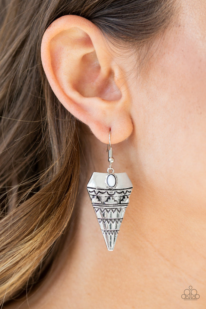 Stamped and embossed in tribal inspired patterns, an antiqued triangular frame swings from the ear. A dainty white bead is pressed into the top of the frame for a refreshing splash of color. Earring attaches to a standard fishhook fitting.  Sold as one pair of earrings.