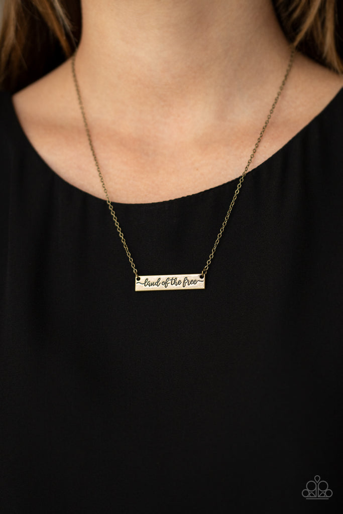 Stamped in the phrase, "Land of the free," a brass rectangular frame is suspended by a dainty brass chain below the collar for a patriotic inspired look. Features an adjustable clasp closure.  Sold as one individual necklace. Includes one pair of matching earrings.
