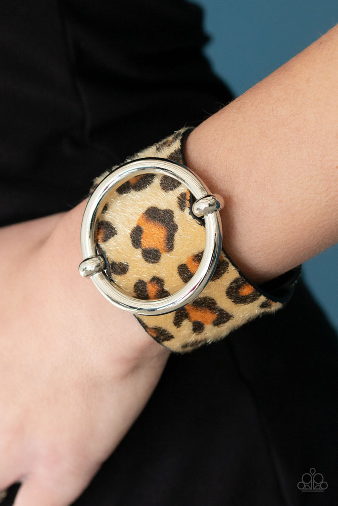 A dramatically oversized silver ring slides along a thick black leather band featuring fuzzy brown cheetah print for a wild finish. Features an adjustable snap closure.  Sold as one individual bracelet.