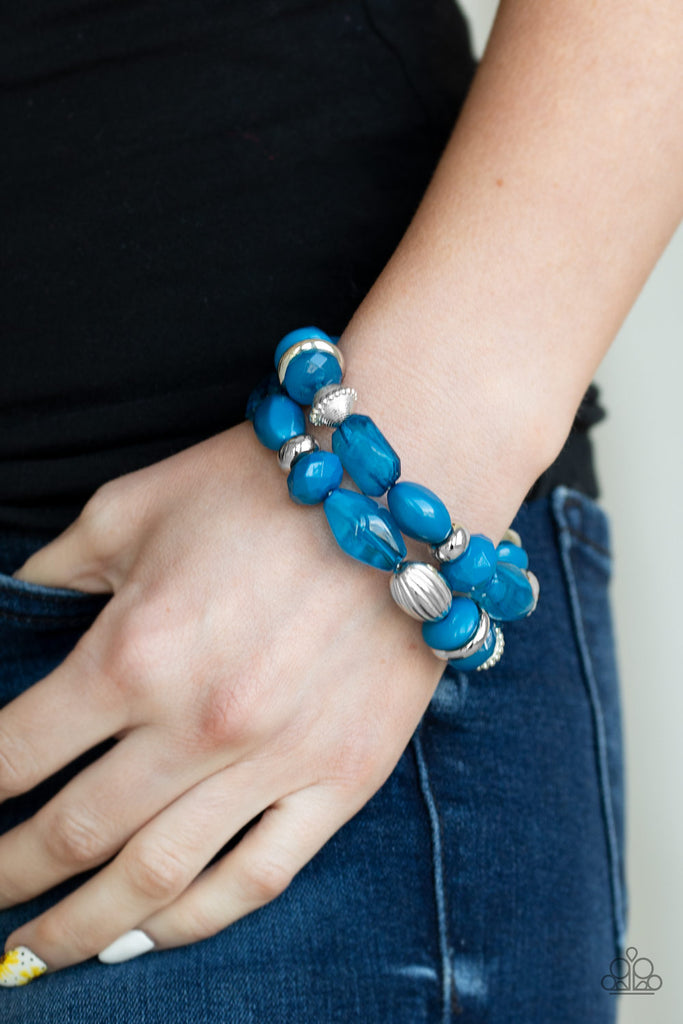 An assortment of opaque, polished blue, and shimmery silver beads are threaded along stretchy bands around the wrist, creating colorful layers.  Sold as one set of two bracelets.