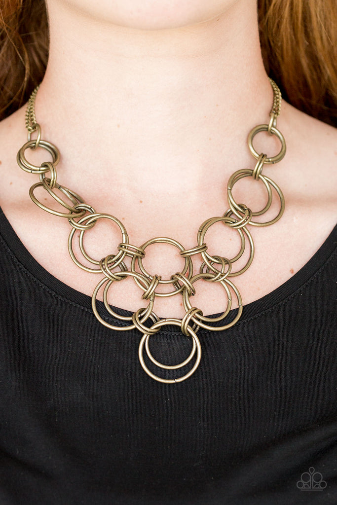 Brushed in an antiqued shimmer, brass rings link together below the collar, creating a bold interlocking pendant. Features an adjustable clasp closure.  Sold as one individual necklace. Includes one pair of matching earrings.