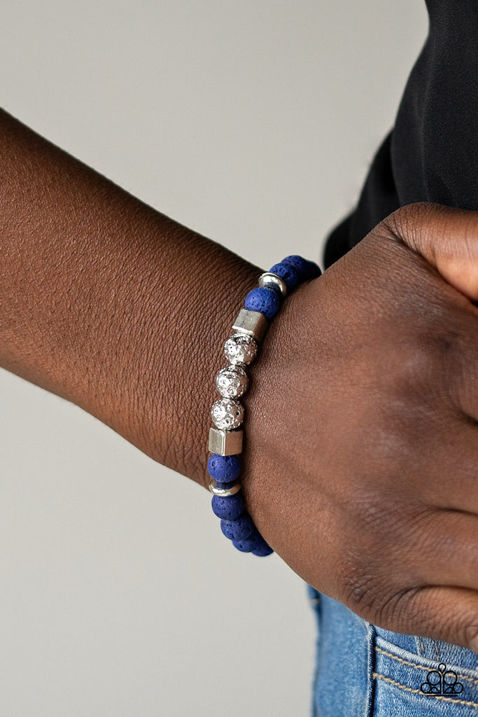 A collection of blue lava rock beads, silver cube beads, and hammered silver beads are threaded along a stretchy band around the wrist for a seasonal flair.  Sold as one individual bracelet.