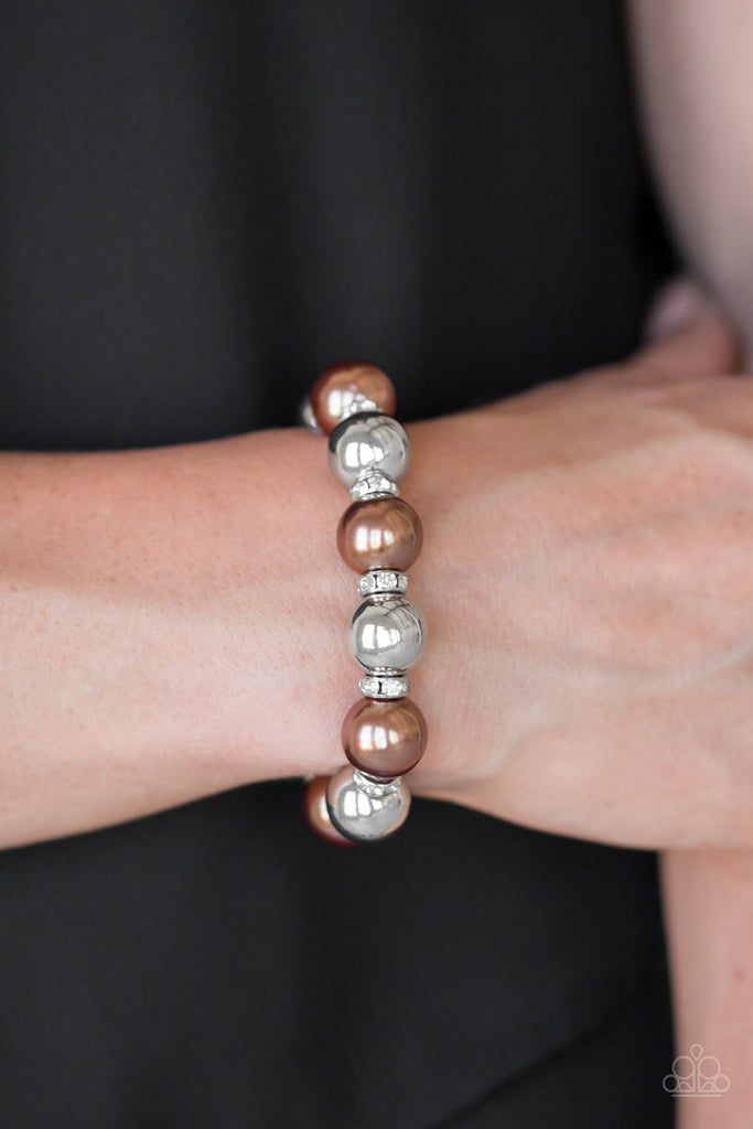 A collection of white rhinestone encrusted rings, brown pearls, and classic silver beads are threaded along a stretchy band around the wrist for a glamorous look.  Sold as one individual bracelet.  