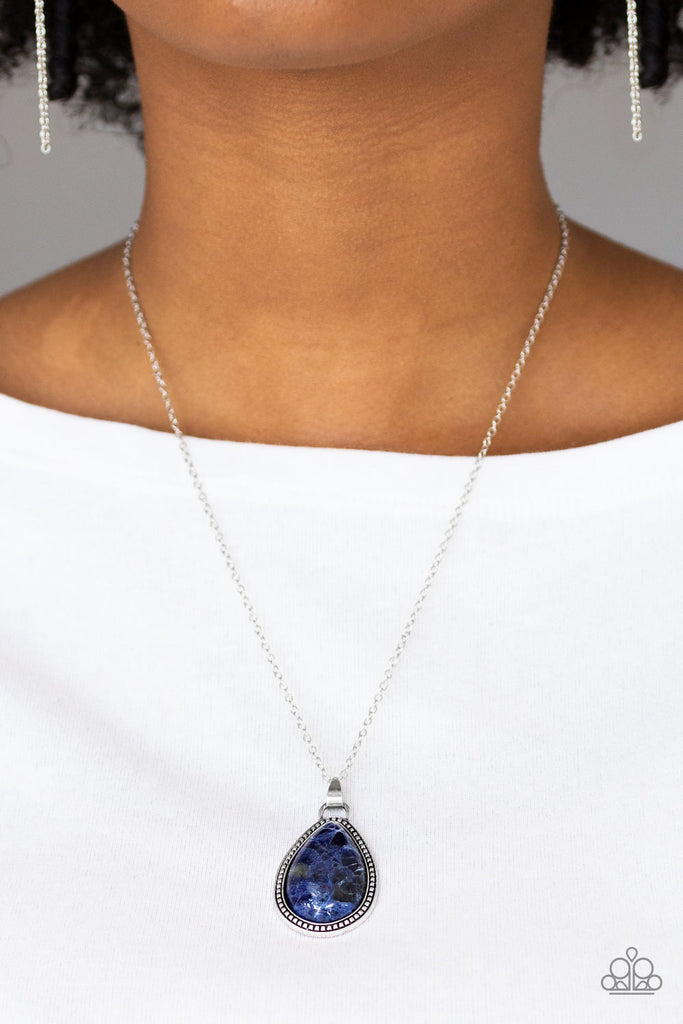 A teardrop blue stone is pressed into a studded silver frame, creating a tranquil pendant below the collar. Features an adjustable clasp closure.  Sold as one individual necklace. Includes one pair of matching earrings.