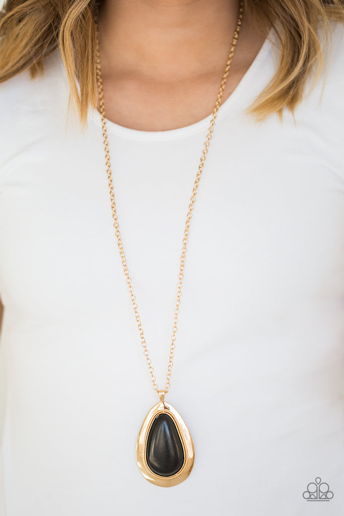 A dramatic black stone teardrop is pressed into a glistening gold frame radiating with rustic patterns. The impressive pendant swings from the bottom of a lengthened gold chain for a seasonal look. Features an adjustable clasp closure.  Sold as one individual necklace. Includes one pair of matching earrings.  