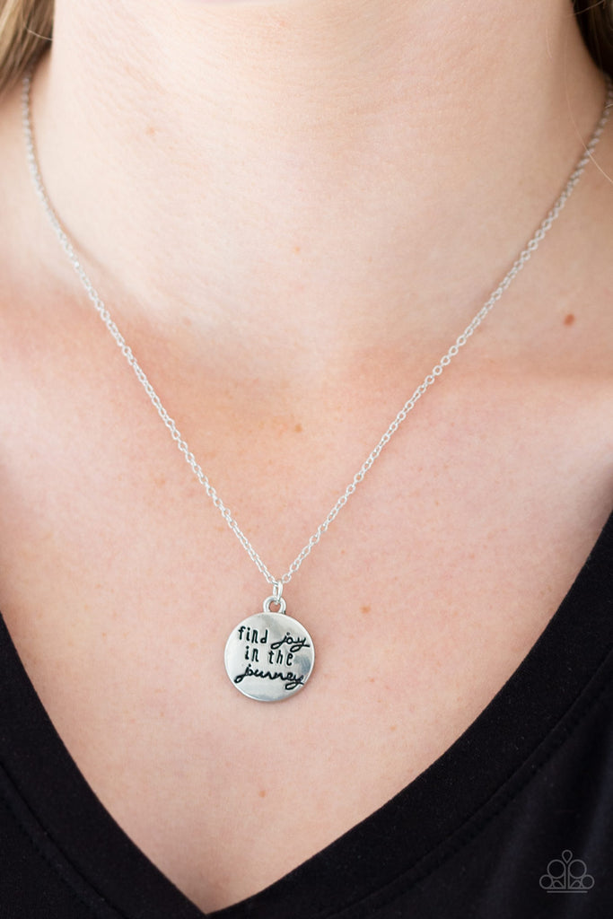 Stamped in the inspirational phrase, "find joy in the journey," a round silver pendant swings below the collar for a seasonal look. Features an adjustable clasp closure.  Sold as one individual necklace. Includes one pair of matching earrings.