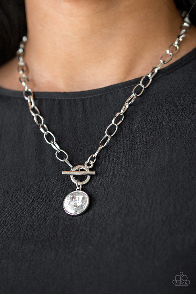 A dramatic gem white swings from the bottom of a shiny silver chain, creating a blinding pendant below the collar. Features a toggle closure.  Sold as one individual necklace. Includes one pair of matching earrings.