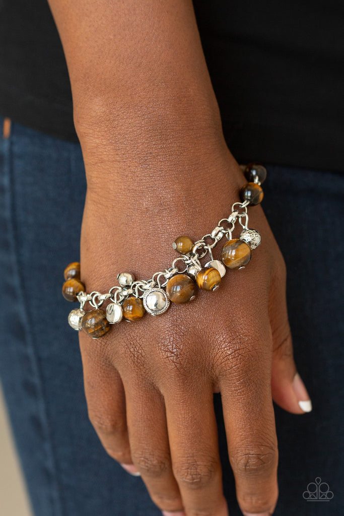 An array of mismatched silver charms and beads swings from a glassy brown beaded bracelet around the wrist, creating a whimsical fringe. Features an adjustable clasp closure.  Sold as one individual bracelet.