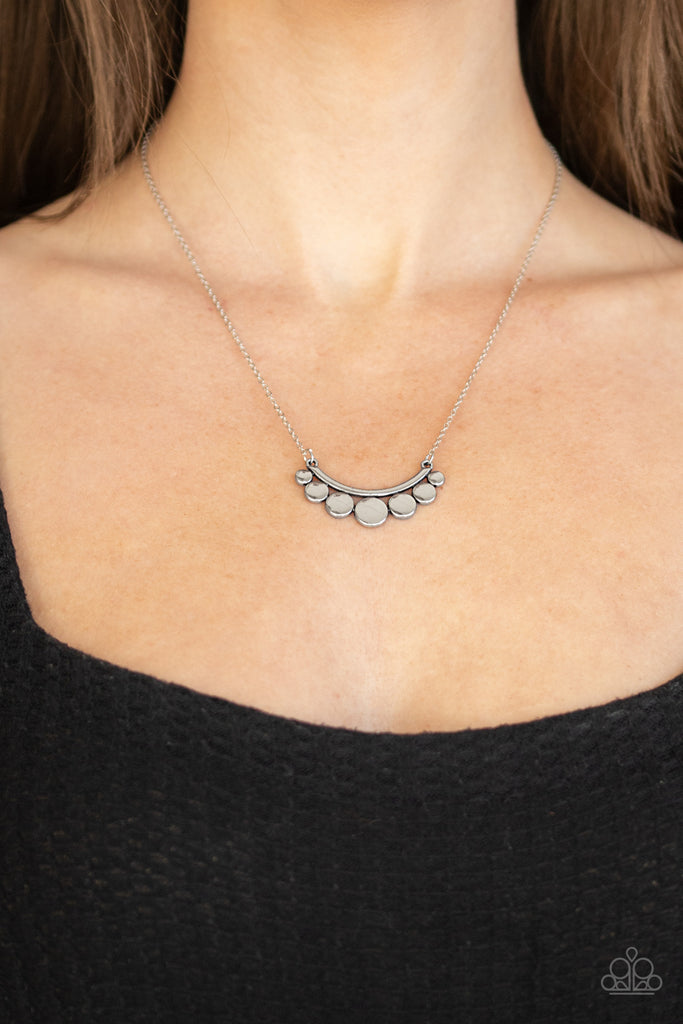 Brushed in an antiqued silver finish, silver discs gradually increase in size at the center as they delicately collect at the bottom of a bowing silver bar. The dainty pendant swings below the collar for a whimsical finish. Features an adjustable clasp closure.  Sold as one individual necklace. Includes one pair of matching earrings.