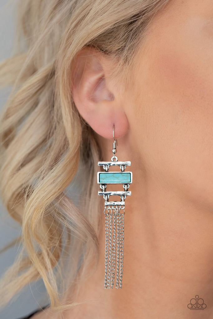 Infused with a flat turquoise stone frame, hammered silver bars stack into an abstract lure. Shimmery silver chains stream from the bottom, creating a whimsical fringe. Earring attaches to a standard fishhook fitting.  Sold as one pair of earrings.