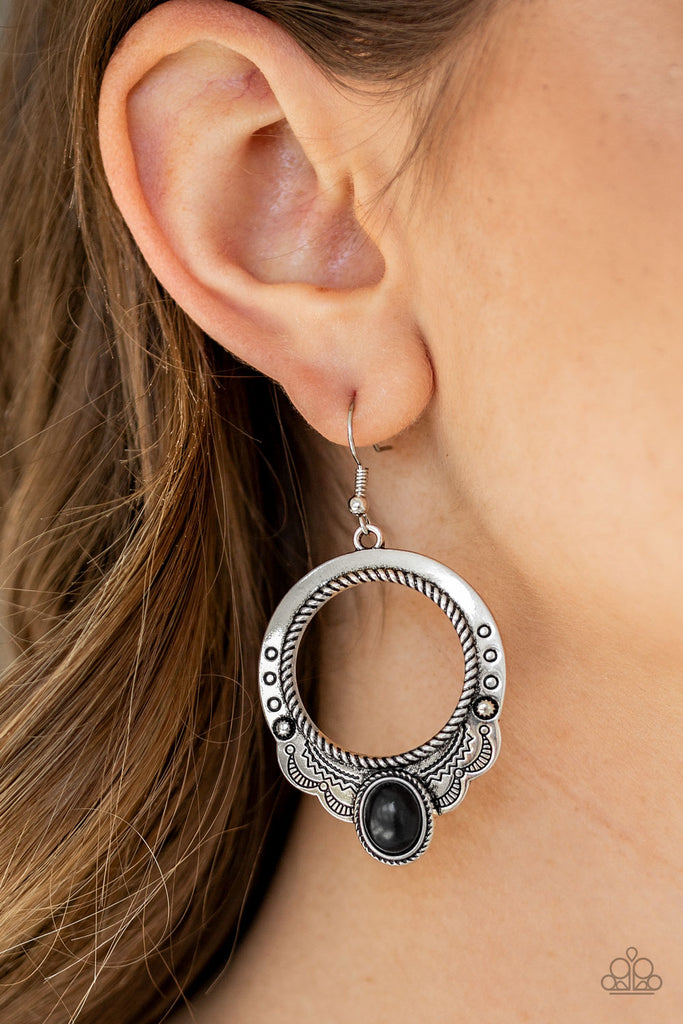 An oval black stone is pressed into the bottom of a scalloped silver hoop stamped and studded in trendy patterns for a southwestern inspired look. Earring attaches to a standard fishhook fitting.  Sold as one pair of earrings.  