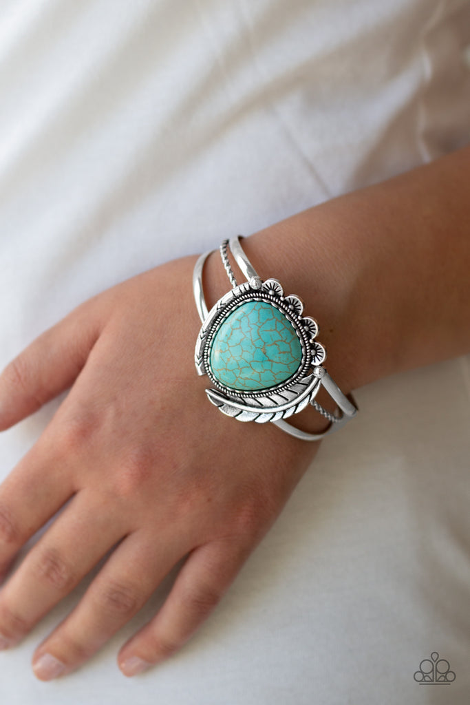 Chiseled into a tranquil teardrop shape, a refreshing turquoise stone is pressed into the center of a layered silver cuff. Stamped in tribal inspired patterns, mismatched silver frames and an antiqued silver feather wraps around the stone center for a seasonal flair.  Sold as one individual bracelet.  