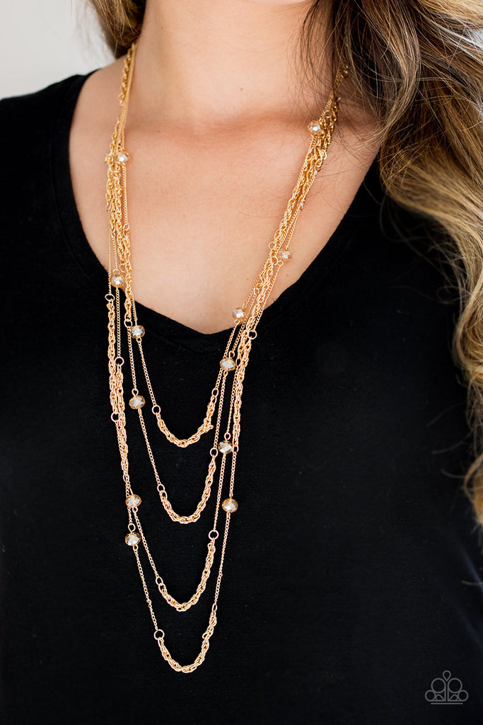 Golden crystal-like beads trickle along three mismatched gold chains, creating shimmery layers across the chest. Features an adjustable clasp closure.  Sold as one individual necklace. Includes one pair of matching earrings.  