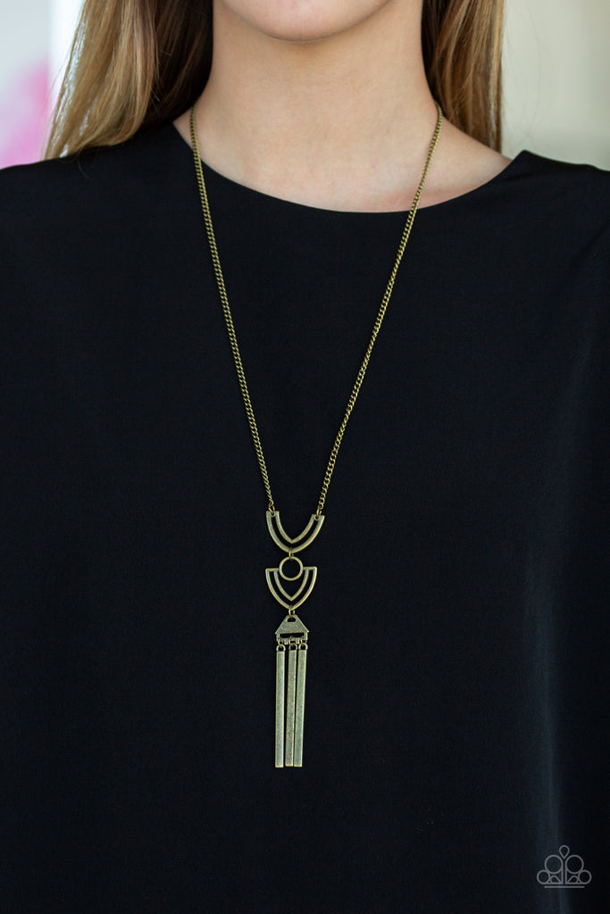 Two airy geometric brass frames link at the bottom of a lengthened brass chain, creating a stacked pendant. Rectangular bars swing from the bottom of the pendant, adding a bold movement to the tribal inspired piece. Features an adjustable clasp closure.  Sold as one individual necklace. Includes one pair of matching earrings.
