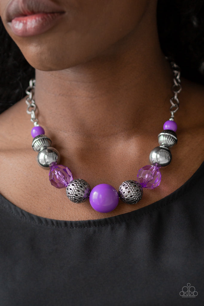 A collection of antiqued silver beads, glassy purple crystal-like beads, and oversized purple beads are threaded along an invisible wire below the collar. Textured in linear patterns, an antiqued silver chain attaches to the colorful compilation for a statement-making finish. Features an adjustable clasp closure.  Sold as one individual necklace. Includes one pair of matching earrings.  