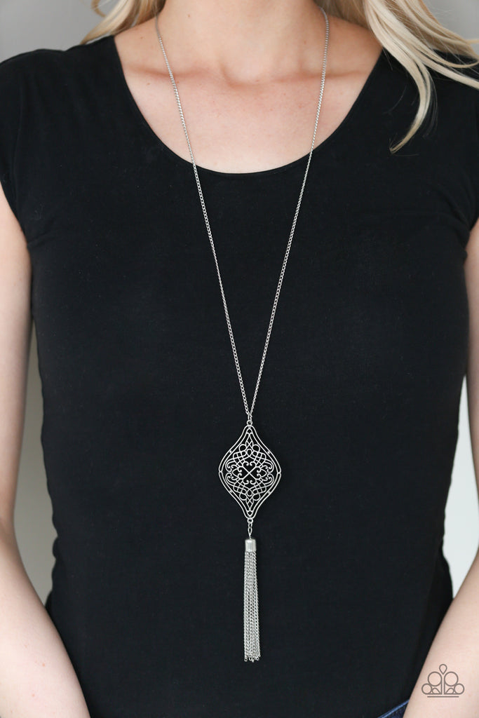 Swirling with whimsical filigree detail, an ornate silver frame swings from the bottom of a lengthened silver chain. A shimmery chain tassel is added for a wanderlust flair. Features an adjustable clasp closure.  Sold as one individual necklace. Includes one pair of matching earrings.