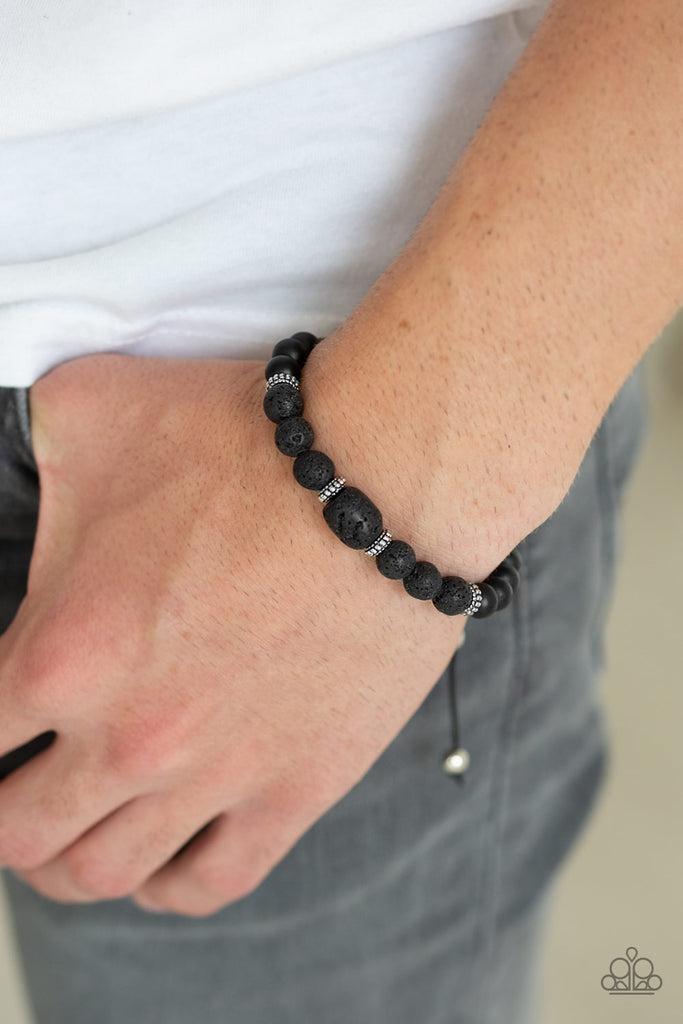 A collection of black lava rock beads, smooth black stones, and dainty silver accents are threaded along a cord around the wrist for a seasonal look. Features an adjustable sliding knot closure.  Sold as one individual bracelet.  
