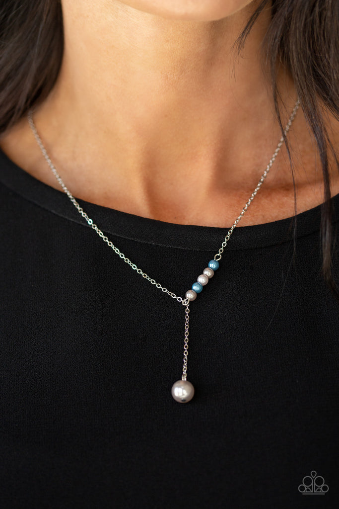 A solitaire silver pearl swings from the bottom of a glistening silver chain, creating a timeless extended pendant below the collar. A section of dainty silver and blue pearls dot one side of the chain for a refined asymmetrical finish. Features an adjustable clasp closure.  Sold as one individual necklace. Includes one pair of matching earrings.  