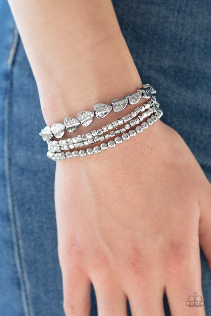 A collection of silver cubes, classic silver beads, and hammered spade-like beading is threaded along stretchy bands around the wrist for a boldly stacked look.  Sold as one set of three bracelets.