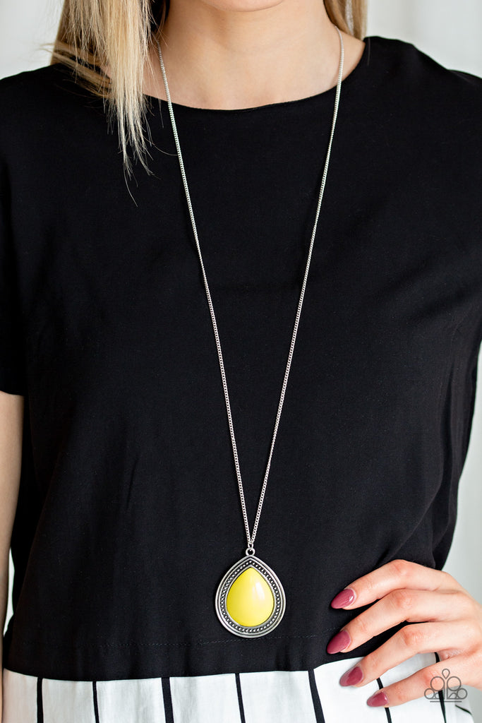 An oversized yellow bead is pressed into the center of a studded teardrop frame, creating a vibrant pop of color at the bottom of a lengthened silver chain. Features an adjustable clasp closure.  Sold as one individual necklace. Includes one pair of matching earrings.