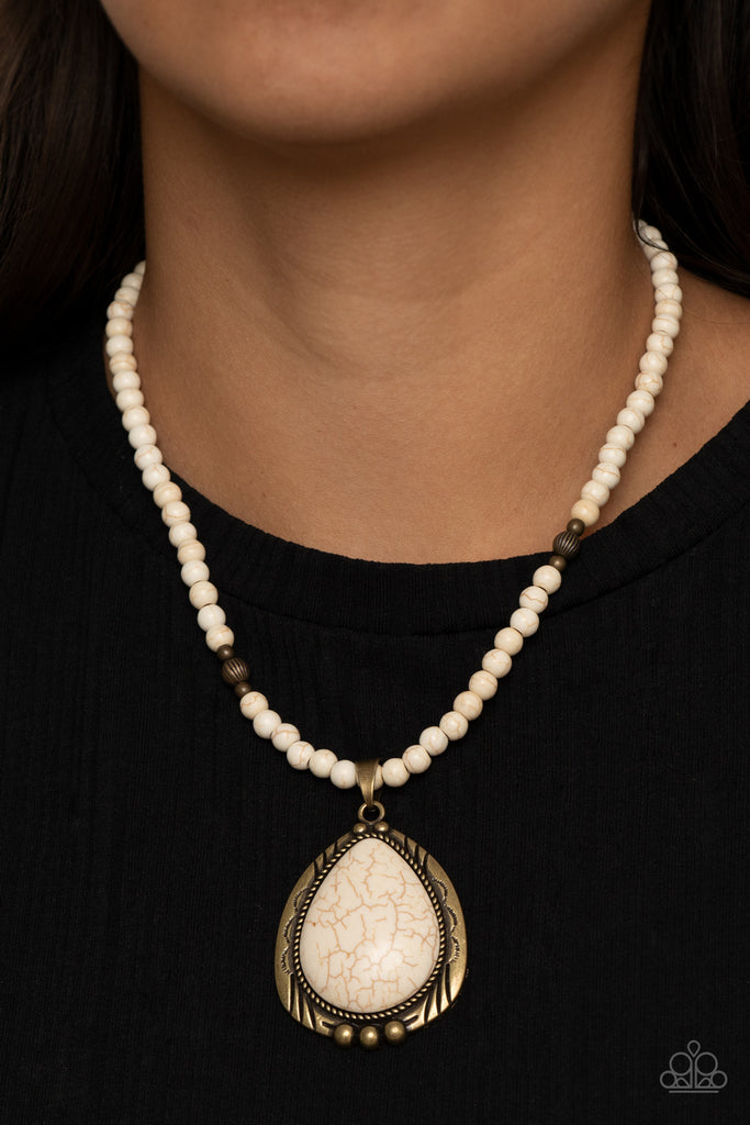 An oversized white stone teardrop is pressed into the center of an ornate brass frame that is studded and stamped in tribal inspired patterns. The rustic pendant glides along an earthy strand of white stone and antiqued brass beads below the collar for a seasonal finish. Features an adjustable clasp closure.  Sold as one individual necklace. Includes one pair of matching earrings.