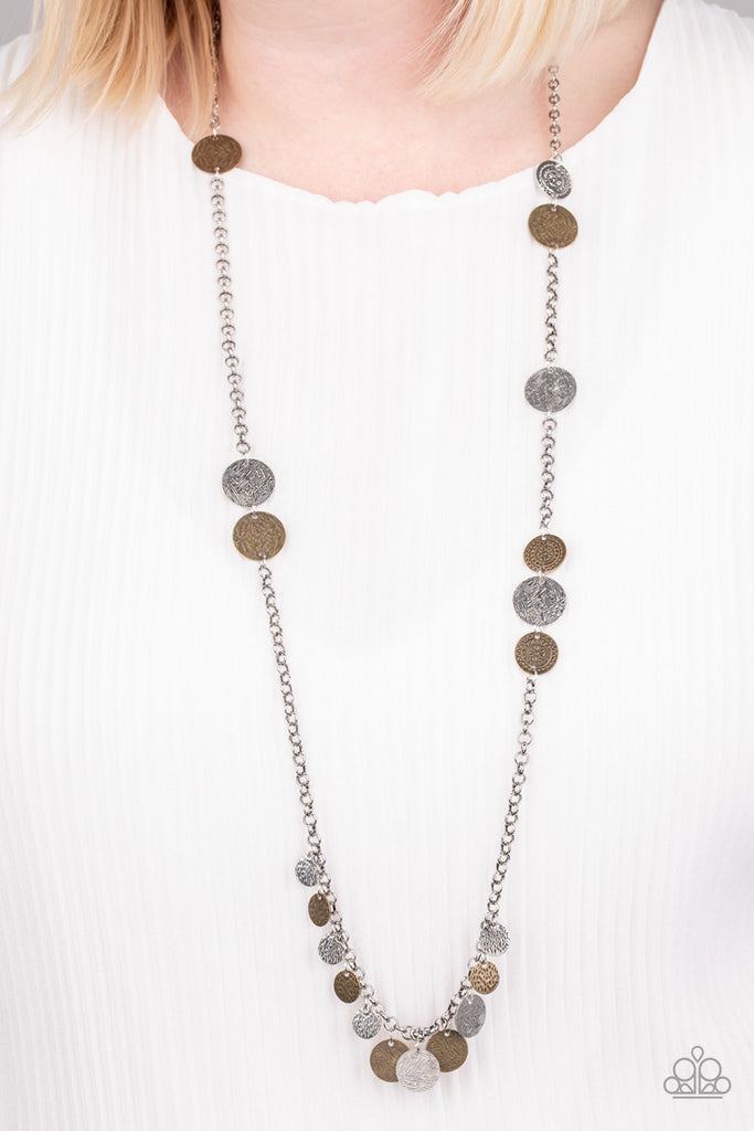 Floral stamped and scratched brass and silver discs trickle along a lengthened silver chain. Hammered and scratched discs dangle from the bottom, creating a noisy fringe. Features an adjustable clasp closure.  Sold as one individual necklace. Includes one pair of matching earrings.  