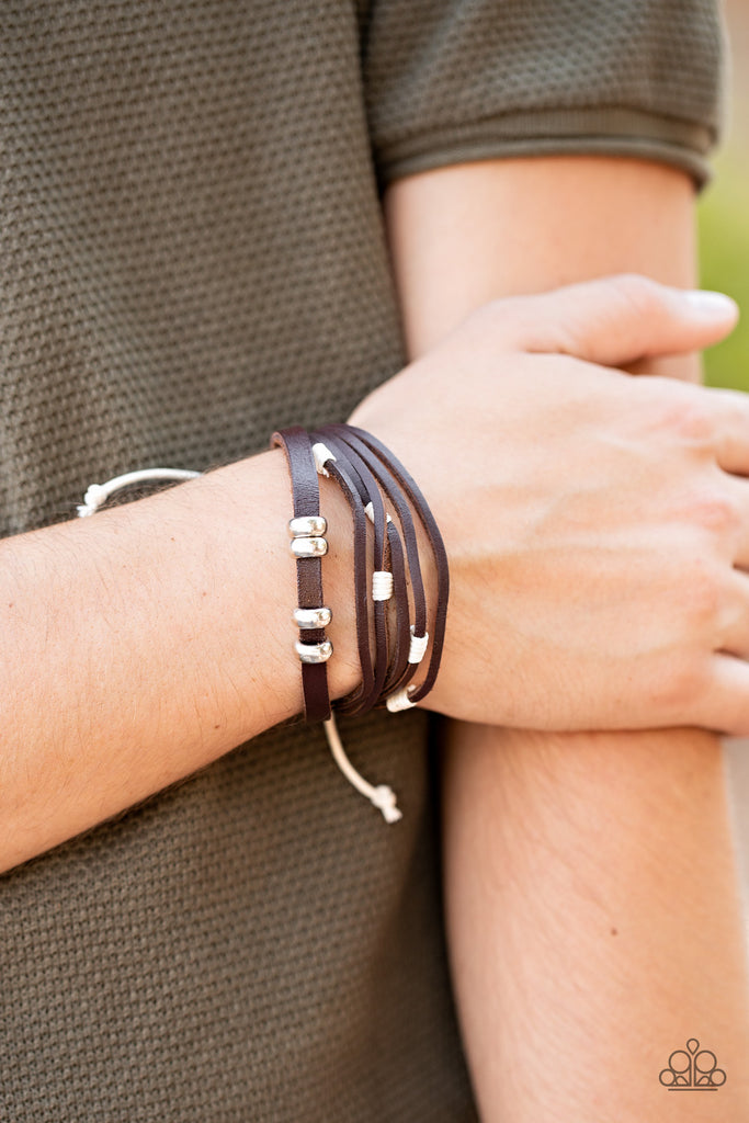 Featuring white threaded and silver beaded accents, mismatched strands of brown leather bands layer across the wrist for an earthy flair. Features an adjustable sliding knot closure.  Sold as one individual bracelet.  