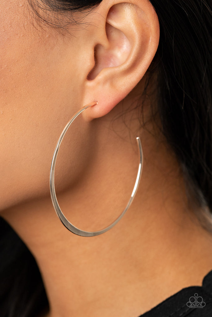 The bottom of a dainty silver hoop is flattened, adding extra sheen to the exaggerated oval curve. Earring attaches to a standard post fitting. Hoop measures approximately 2 1/4" in diameter.  Sold as one pair of hoop earrings.  