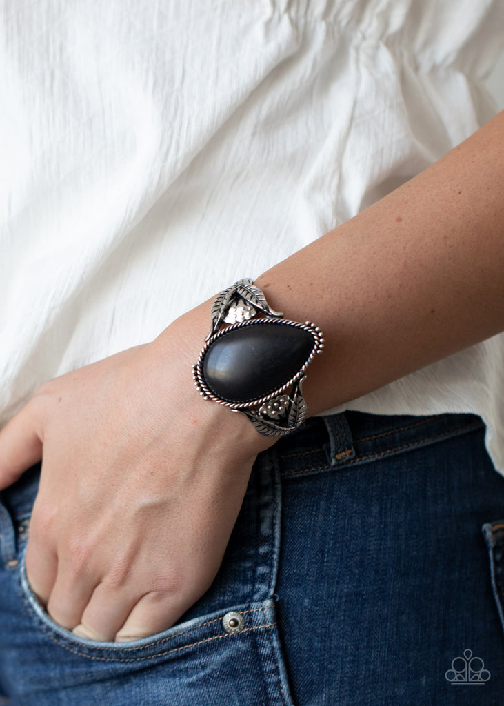 Encased in a silver rope-like frame, an oversized black teardrop stone is pressed into the center of an airy silver cuff abloom with leafy floral designs.  Sold as one individual bracelet.  