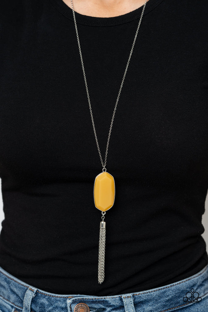 Featuring a faceted surface, a dewy yellow acrylic gem swings from the bottom of a lengthened silver chain. A shimmery silver chain tassel attaches to the bottom of the colorful pendant, adding flirtatious movement. Features an adjustable clasp closure.  Sold as one individual necklace. Includes one pair of matching earrings.  
