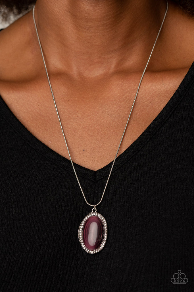 Encrusted with a ring of glittery white rhinestones, a wavy silver frame nestles around a glassy purple cat's eye stone. The dewy frame slides along a rounded silver snake chain, creating a glistening pendant below the collar. Features an adjustable clasp closure.  Sold as one individual necklace. Includes one pair of matching earrings.