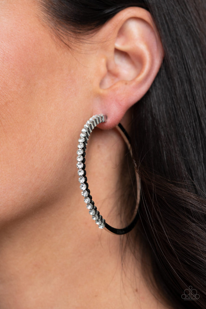 The front half of a glistening silver hoop is encrusted in a glassy row of dainty white rhinestones for a glamorously timeless finish. Earring attaches to a standard post fitting. Hoop measures approximately 2 1/2" in diameter.  Sold as one pair of hoop earrings.