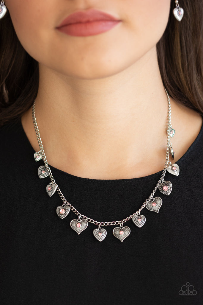 Dotted with glittery pink rhinestone centers, a mismatched collection of silver heart frames swing from a dainty silver chain below the collar, creating a flirtatious fringe. Features an adjustable clasp closure.  Sold as one individual necklace. Includes one pair of matching earrings.