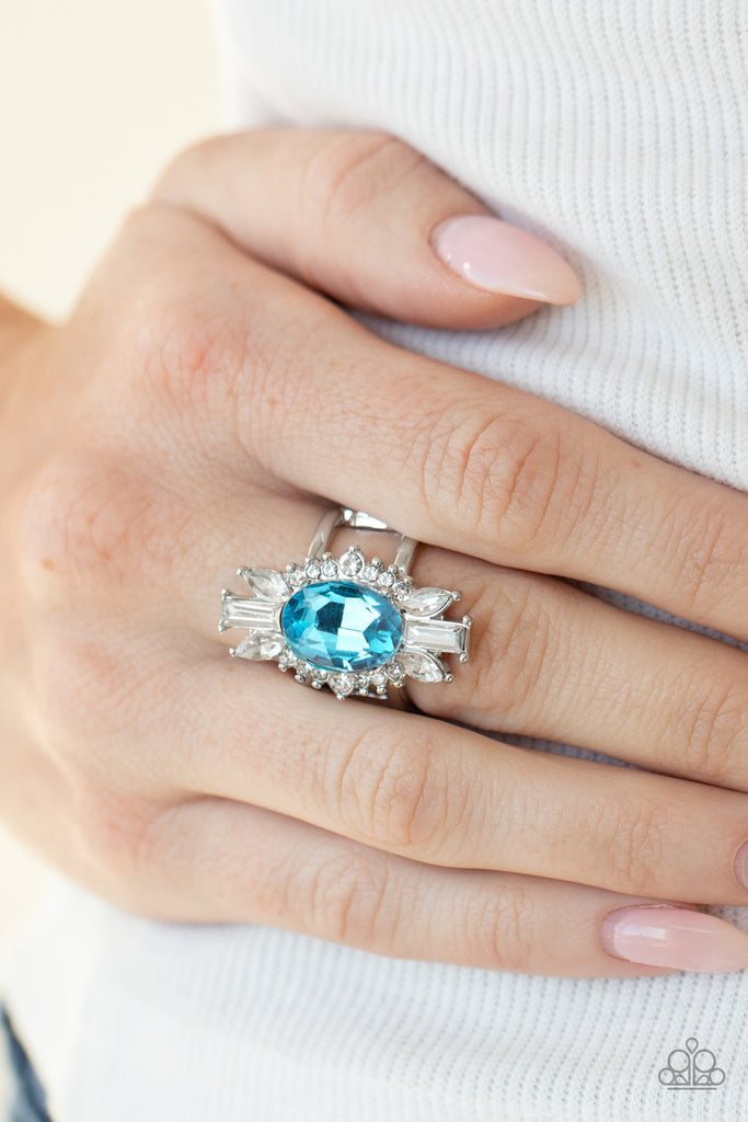 An icy collection of round, marquise, and emerald style white rhinestones radiate out from a blue gem center, creating a glamorous centerpiece atop the finger. Features a stretchy band for a flexible fit.  Sold as one individual ring.  