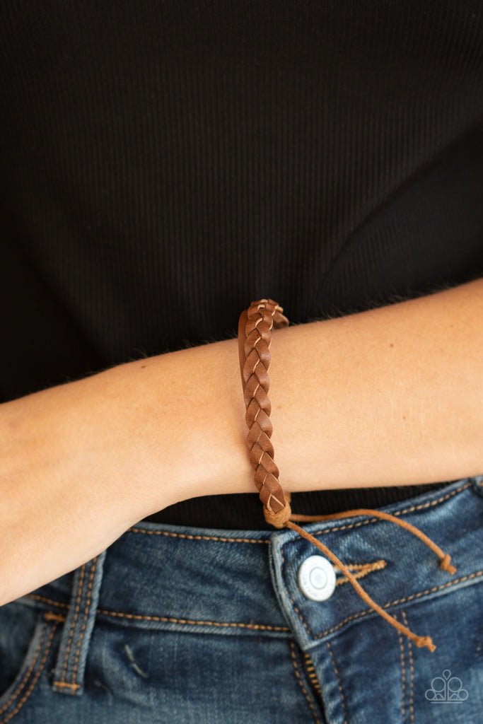 Strands of brown leather cording braid across the front of a dainty leather band, creating a rustic display around the wrist. Features an adjustable sliding knot closure.  Sold as one individual bracelet.  