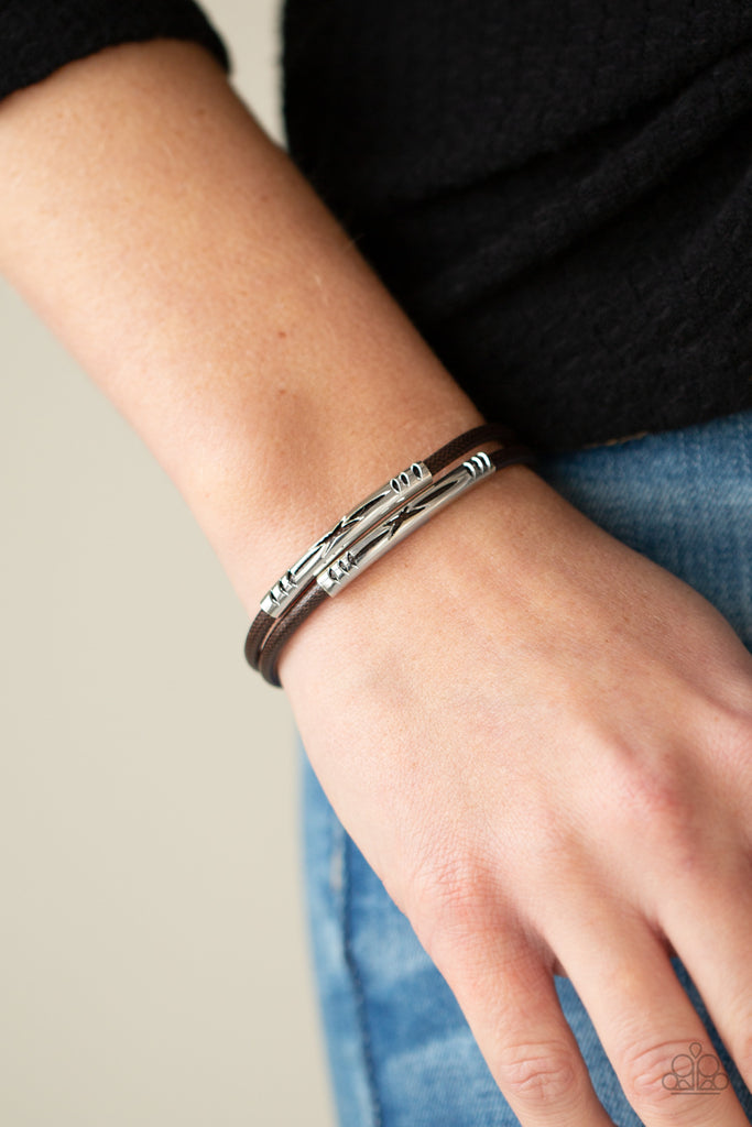 Featuring tribal inspired cutouts, stenciled silver bars slide along two shiny brown cords around the wrist for an adventurous look. Features a magnetic closure.  Sold as one individual bracelet.