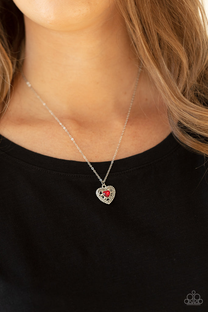 Bordered in dainty white rhinestones, an airy silver locket inspired pendant is dotted with a red heart-shaped rhinestone as it flirtatiously glides along a dainty silver chain below the collar. Features an adjustable clasp closure.  Sold as one individual necklace. Includes one pair of matching earrings.