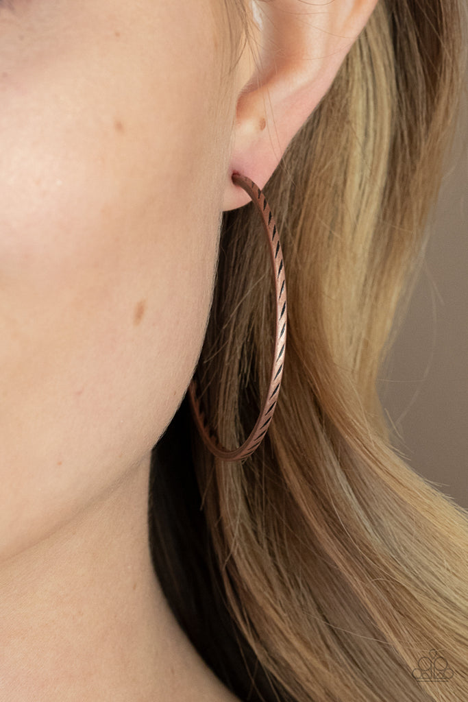 Etched in a subtle slanted texture, a dainty copper hoop delicately curves around the ear in a rustic finish. Earring attaches to a standard post fitting. Hoop measures approximately 2” in diameter.  Sold as one pair of hoop earrings.  