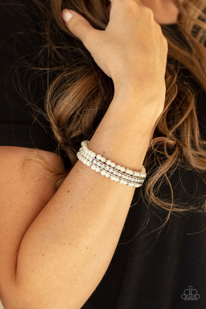 Threaded along stretchy bands, three rows of dainty white pearls are held in place around the wrist by a white rhinestone encrusted centerpiece for a romantic flair.  Sold as one individual bracelet.