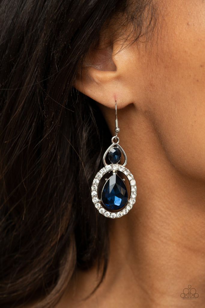 An oversized blue teardrop gem is nestled inside a ring of glassy white rhinestones that attaches to an airy silver fitting adorned with a blue oval rhinestone. Earring attaches to a standard fishhook fitting.  Sold as one pair of earrings.  