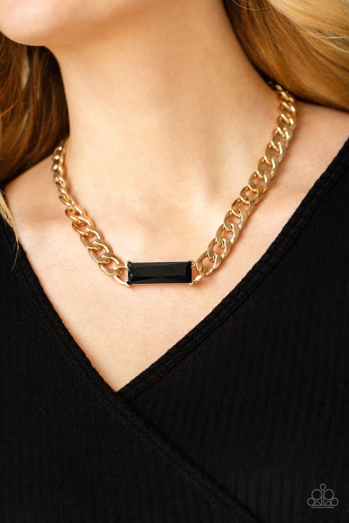 A dramatically oversized row of gold chain attaches to a black emerald cut rhinestone pendant, creating a demanding centerpiece below the collar. Features an adjustable clasp closure.  Sold as one individual necklace. Includes one pair of matching earrings.