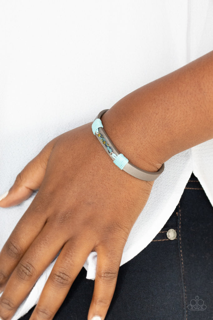 Threaded along a dainty rod, a row of metallic and iridescent blue cube beads are knotted in place across the center of a silvery leather band. Features an adjustable snap closure.  Sold as one individual bracelet.