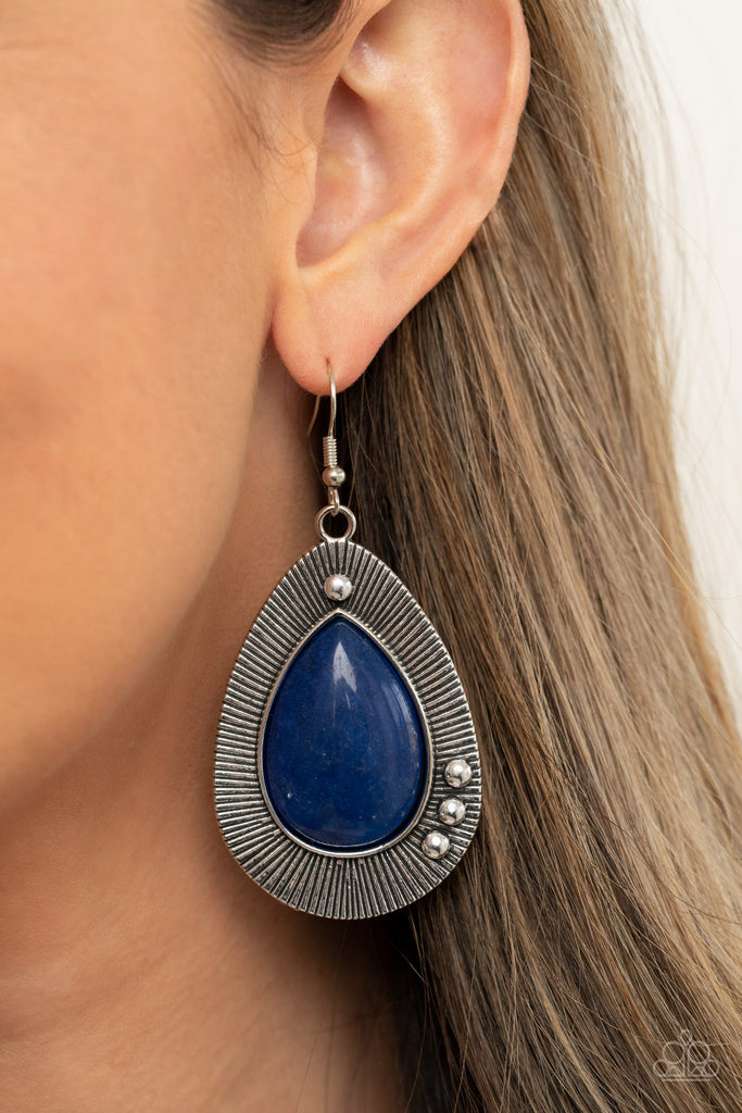 Chiseled into a tranquil teardrop, a shimmery French Blue stone bead is pressed into the center of a rustically studded silver frame radiating with antiqued detail for a southwestern flair. Earring attaches to a standard fishhook fitting.  Sold as one pair of earrings.