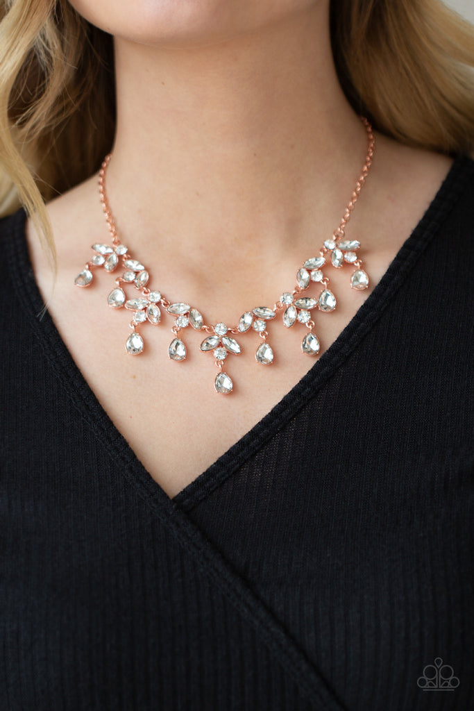 Adorned in glassy white rhinestones, leafy shiny copper frames delicately connect below the collar. Classic white teardrop rhinestones drip from the elegant foliage, adding dazzling movement to the timeless display. Features an adjustable clasp closure.  Sold as one individual necklace. Includes one pair of matching earrings.  