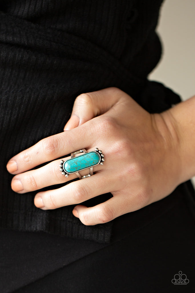 An oblong turquoise stone is pressed into a sleek silver frame featuring a studded top and bottom. The rustic frame sits atop two layered bands, creating a whimsical centerpiece atop the finger. Features a stretchy band for a flexible fit.  Sold as one individual ring.